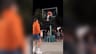 Middle Finger Dunk AI trend: a dunker in a black jacket flying over a defender in an orange hoodie on a floodlit night court