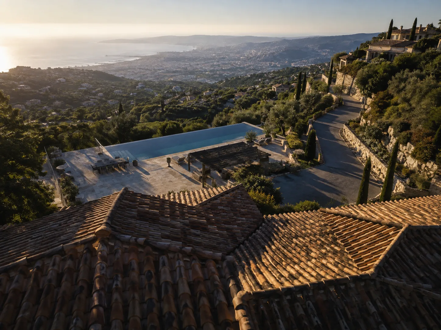 Aerial crane reveal rising over a hillside villa roofline to show the infinity pool and the coastal town below — a real estate drone video shot