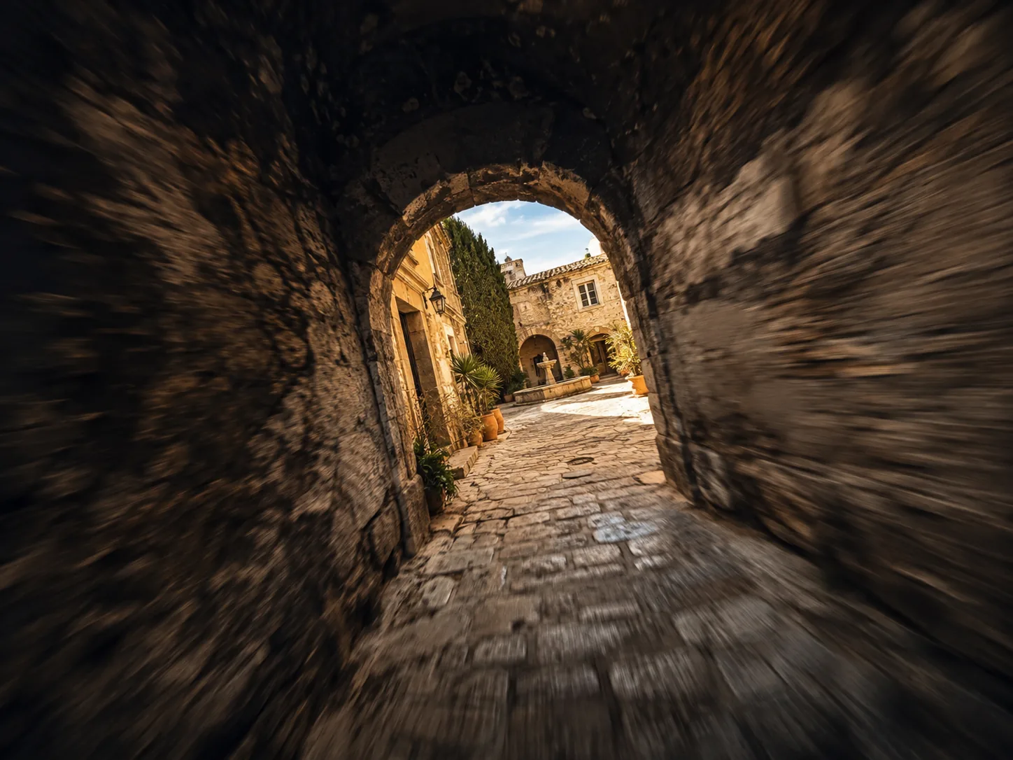 FPV drone fly-through racing under a stone archway into a sunlit courtyard, walls blurred by speed