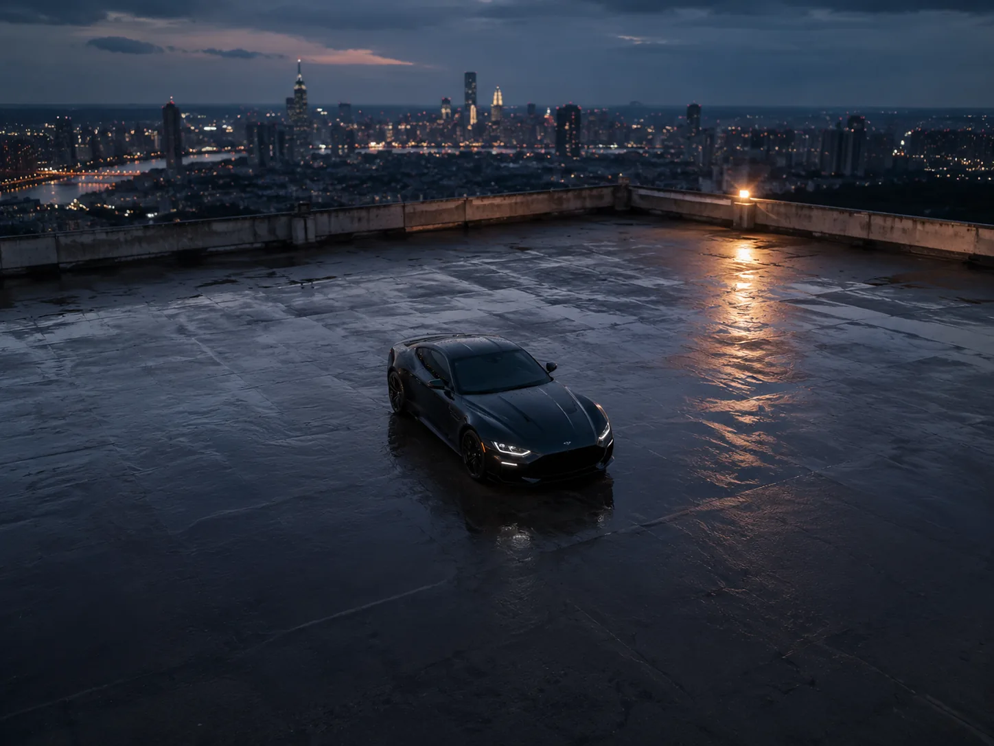 360-degree drone orbit shot circling a black sports car alone on a wet rooftop at blue hour, city skyline behind