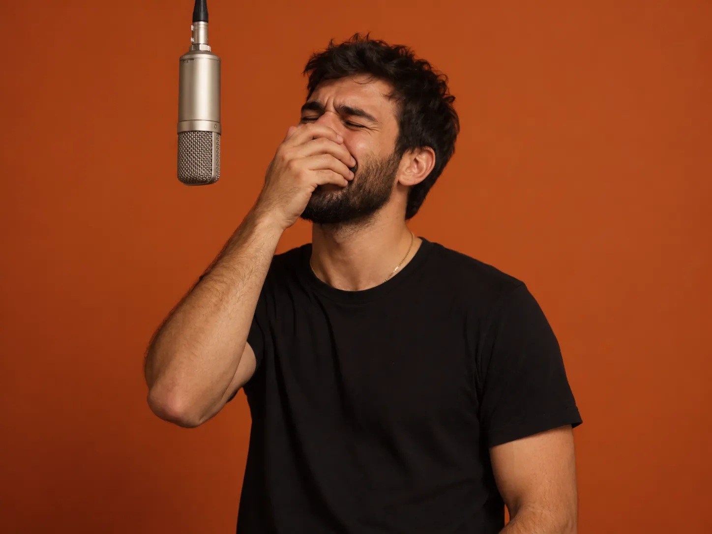 A bearded man in a black T-shirt squeezes his eyes shut and holds a hand over his mouth while singing at a hanging studio mic, a Bécane Yamê AI trend video made for a friend