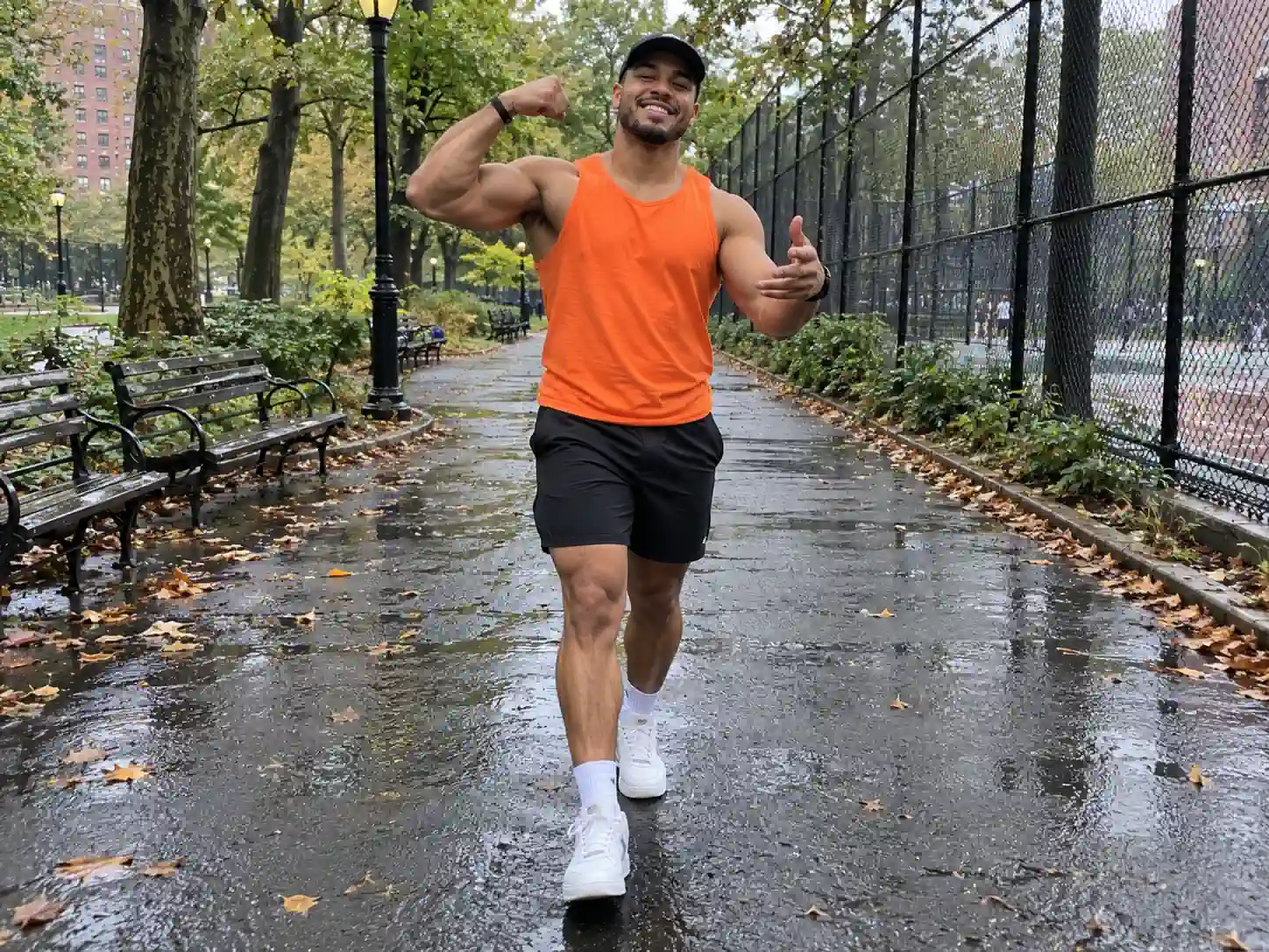 A young man in an orange tank top swaggering down a wet park path toward the camera, a Fergie Baby AI walk video