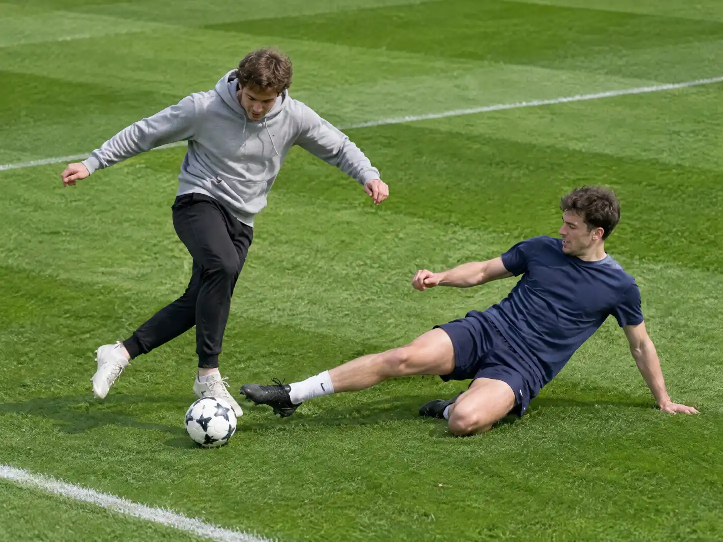 A twenty-something in a grey hoodie faking a rabona on a grass pitch while his friend slides in and misses, a Lamine Yamal rabona AI video with friends