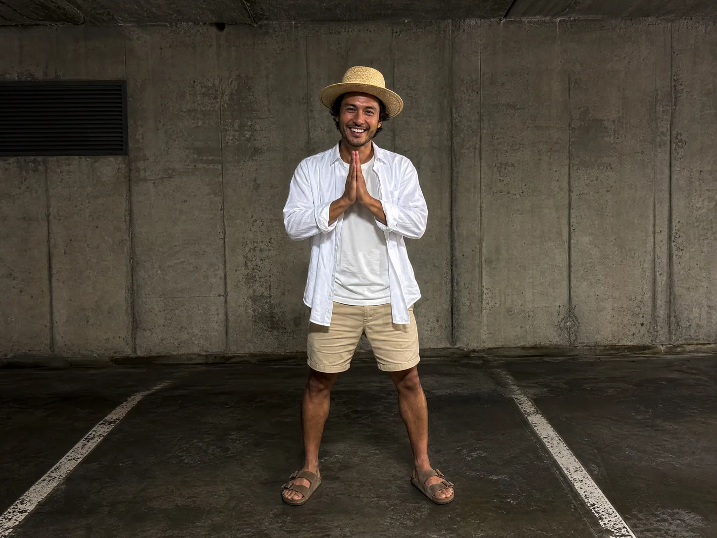 A traveller in a straw sun hat and open linen shirt pressing his palms together in a wai at the end of the SaWaDiKa dance, a Sawadika AI video from a holiday photo