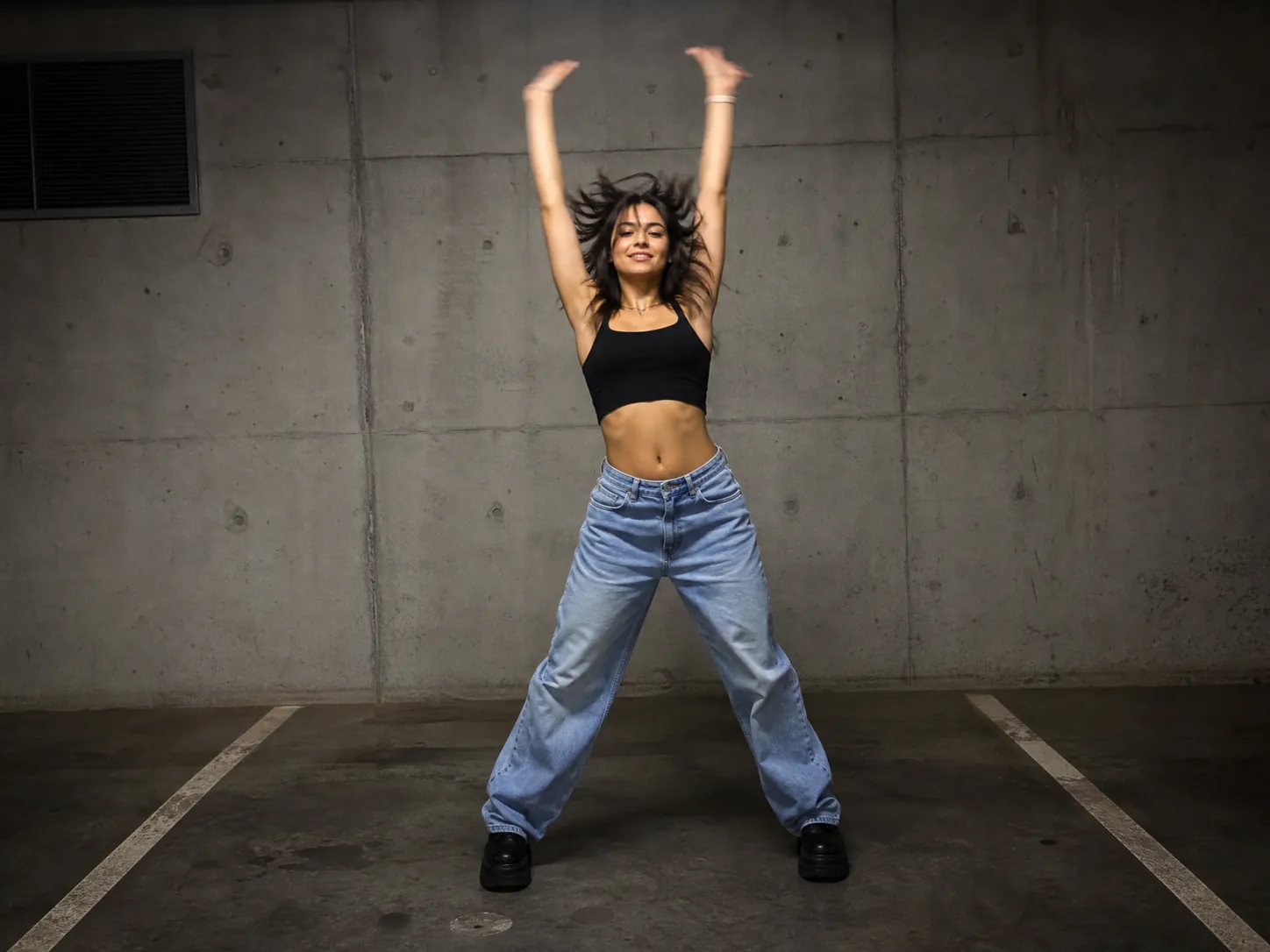 A young woman in a black crop top and baggy light-blue jeans throwing both arms overhead in the SaWaDiKa dance against a concrete wall, a Lisa SaWaDiKa dance AI video