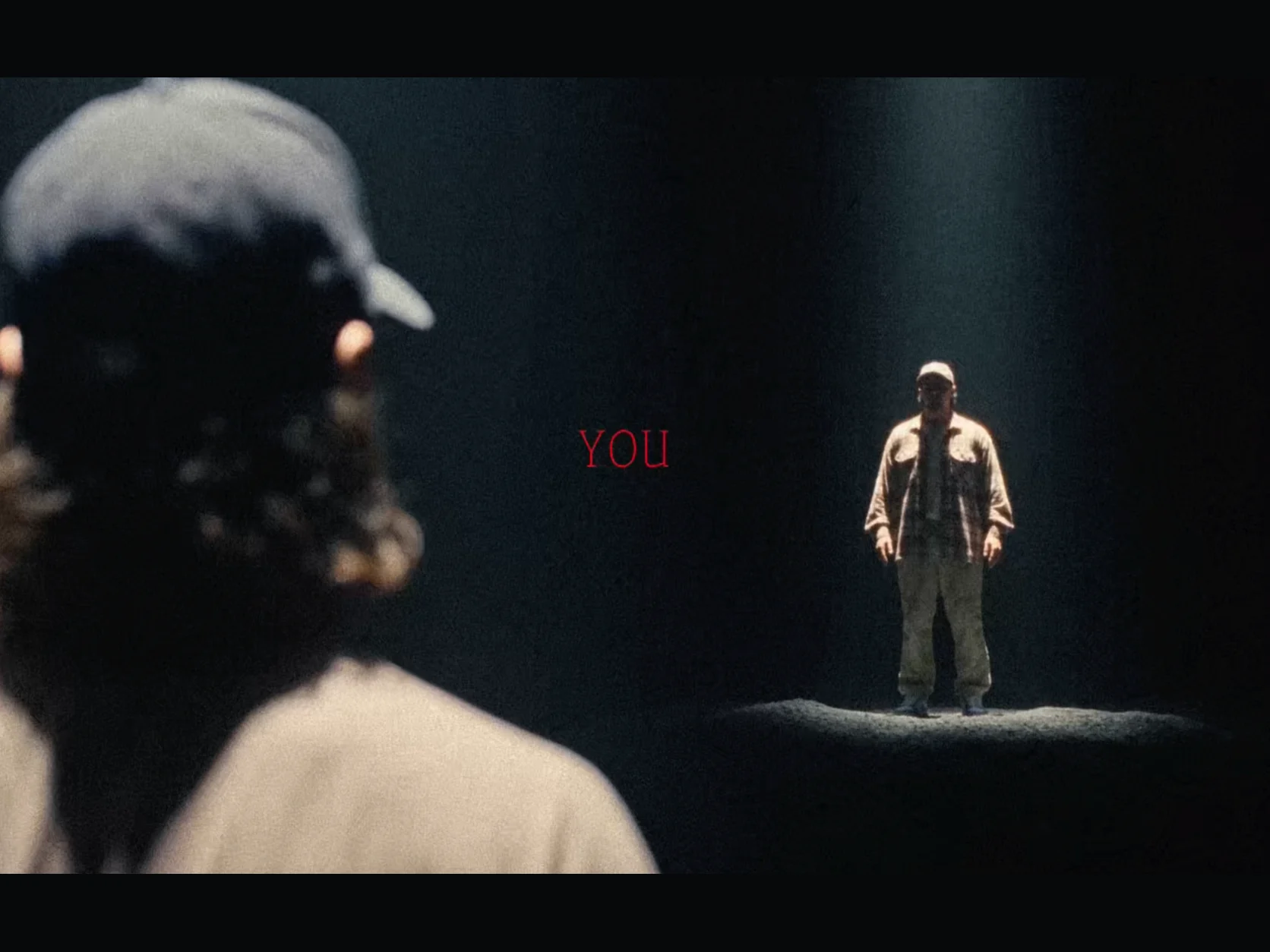 A person seen from behind watching another version of themselves beneath a spotlight with the word YOU between them